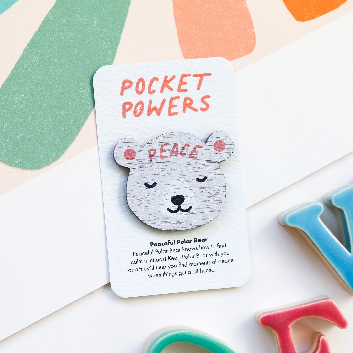 A wooden polar bear token, with the word 'peace' on their forehead. It is stuck to a card that says 'Pocket Powers - Peaceful Polar Bear knows how to find calm in chaos. Keep Polar Bear with you and they'll help you find moments of peace when things get a bit hectic.'