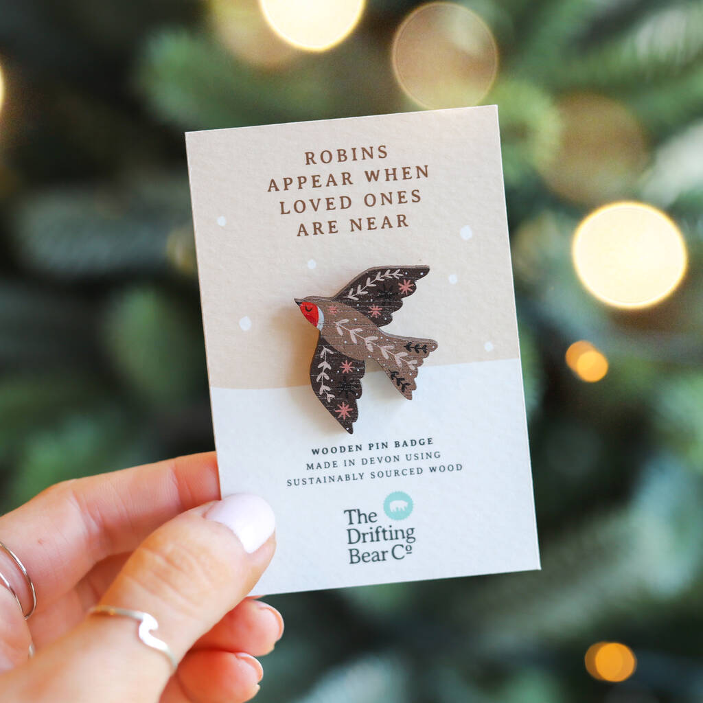 A beautiful wooden pin badge in the shape of a robin, with intricate leaf pattern detailing on the wings and back. It is attached to a rectangular card with the words 'Robins appear when loved ones are near' at the top, and 'wooden pin badge made in devon using sustainably sourced wood' at the bottom.